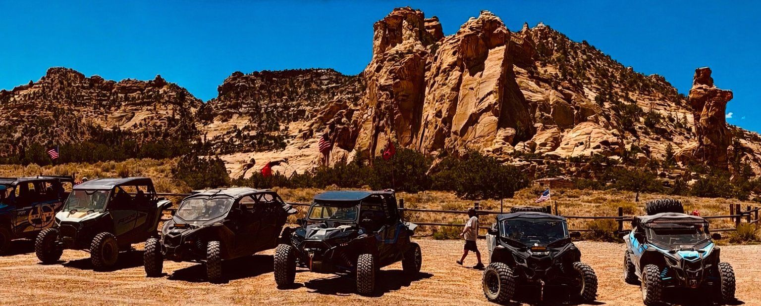 A line of side-by-sides parked below red sandstone cliffs in southern Utah